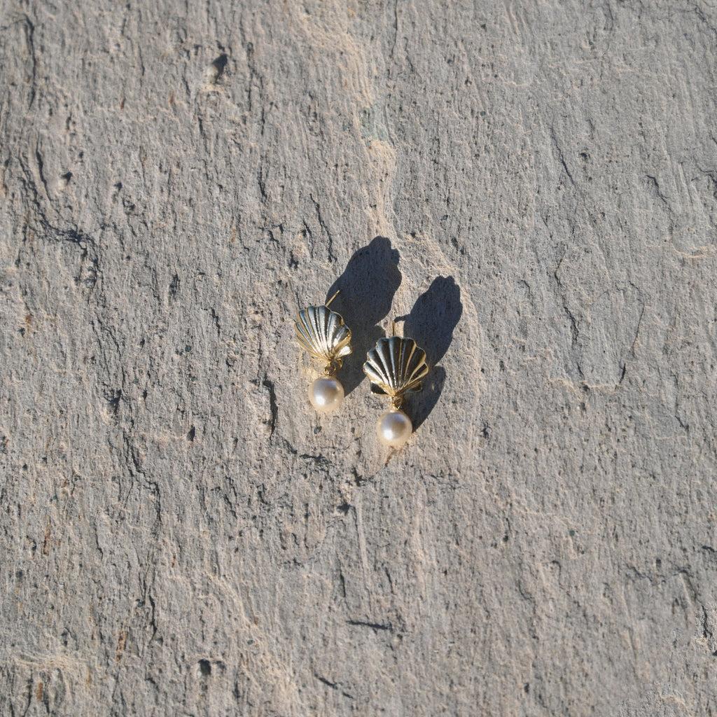 Shell-shaped earrings with pearl-like beads on a textured stone surface